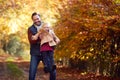 Father Playing Game Picking Up Daughter On Family Walk Along Track In Autumn Countryside