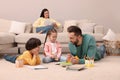 Father playing with his children while mother reading book on sofa in living room Royalty Free Stock Photo