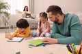 Father playing with his children while mother reading book on sofa in living room Royalty Free Stock Photo