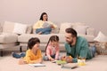 Father playing with his children while mother reading book on sofa in living room Royalty Free Stock Photo