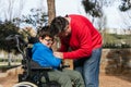 Father playing with his son with disability in a wheelchair while they enjoy time together outdoors in the park.