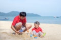 Father playing sand with cute Smiling little Asian 18 months old toddler boy on sand beach on nature outdoor Royalty Free Stock Photo
