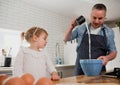 Father pouring ingredients into bowel baking with daughter in organised kitchen.