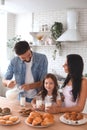 Father pouring milk from the jug into the glasses for daughter and wife in the kitchen Royalty Free Stock Photo