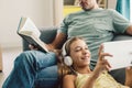 Father and pre teen daughter playing tablet and reading book while relaxing together on couch in room at home Royalty Free Stock Photo