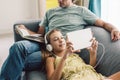 Father and pre teen daughter playing tablet and reading book while relaxing together on couch in room at home Royalty Free Stock Photo
