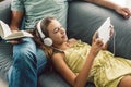 Father and pre teen daughter playing tablet and reading book while relaxing together on couch in room at home Royalty Free Stock Photo