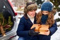 Father presents daughter a gift box on snowy winter day outdoors. Christmas tree in large trunk of family car. Girl Royalty Free Stock Photo