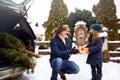 Father presents daughter a gift box on snowy winter day outdoors. Christmas tree in large trunk of family car. Girl Royalty Free Stock Photo