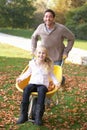 Father pushing child through autumn leaves