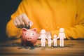 Father putting coins on piggy bank with family icon on the table.