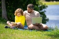 Father read a book with son in a park outdoors. Father and child son reading outdoor on green nature background. Dad Royalty Free Stock Photo