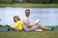 Father reading book with son in park, preparing school homework together, parenting. Summer lifestyle. Parenting and Royalty Free Stock Photo