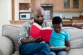 Father reading book while son sitting next to him using digital tablet Royalty Free Stock Photo