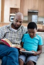 Father reading book while son sitting next to him using digital tablet Royalty Free Stock Photo