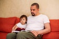 Father reading book to toddler son, child is looking away and thinking. Dad and little son sitting at home and reading fairy tales