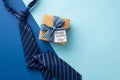 Father`s Day concept. Top view photo of craft paper gift box with striped ribbon bow postcard and blue necktie on bicolor blue Royalty Free Stock Photo