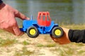 Father's large hand pass plastic toy truck to hand of a little boy. Hands in blue and black shirts.