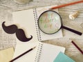 Father`s tools, black paper mustache, magnifying glass, pencils and a greeting inscription in a notebook on a light wooden table