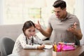 Father scolding his daughter while helping with homework at table