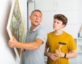 Father shows his son how to hang painting on the wall of house Royalty Free Stock Photo