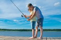 Father shows his son on the pier how to hold a fishing rod to catch fish, against the blue lake and sky Royalty Free Stock Photo