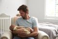 Father Sitting In Nursery Chair Holds Sleeping Baby Son