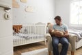 Father Sitting In Nursery Chair Holds Sleeping Baby Son