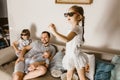 Father is sitting on the sofa with baby on his arms and his two daughters in the special glasses watching tv next to him