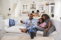 Father Sitting On Sofa Watching TV With Teenage Daughters