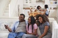 Father Sitting On Sofa Watching TV With Teenage Daughters