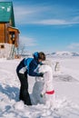 Father and a small child are making a big snowman in the snowy yard of a wooden cottage. Back view Royalty Free Stock Photo