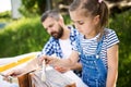 Father with a small daughter outside, painting wooden birdhouse. Royalty Free Stock Photo