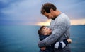 Father with small son on a walk outdoors standing on beach at dusk.