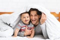 Caucasian man hiding with baby under blanket in bed