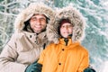 Father and son dressed in Warm Hooded Casual Parka Jacket Outerwear walking in snowy forest cheerful smiling faces portrait. Royalty Free Stock Photo