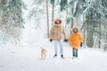 Father and son dressed in Warm Hooded Casual Parka Jacket Outerwear walking in snowy forest with his beagle dog in pine forest. Royalty Free Stock Photo