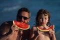 Father and son eat juicy red watermelon on beach. Summer kid holidays, seasonal fruits and berries. Summer father and Royalty Free Stock Photo