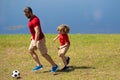 Father and son enjoy a friendly game of football. Practice passing and kicking soccer ball. Father teaches his son play