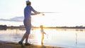 Father and son fishing on the shore of the river at sunset