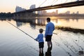 Father and son are fishing together standing with fishing rods in the water of the river at sunset Royalty Free Stock Photo