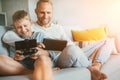 Father and son game players funs sit together at home on cozy sofa, using the tablet and gamepad Royalty Free Stock Photo