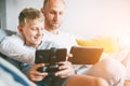 Father and son game players funs sit together using the tablet and gamepad at home on cozy sofa Royalty Free Stock Photo