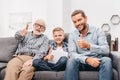 Father, son and grandfather sitting together on couch in living room and showing