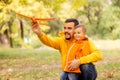 Father and son having fun in autumn park, launching toy airplane outdoors. Yellow trees in background Royalty Free Stock Photo
