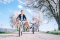 Father and son having fun spreading wide legs and screaming when riding bicycles on country road under blossom trees. Healthy