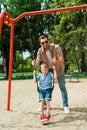 father and son having fun on swing at playground in park and looking Royalty Free Stock Photo