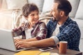 Father and son at home sitting at table dad hugging boy cheerful browsing internet on laptop close-up