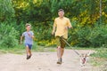 Father and son jogging along country dirt road with dog on waist leash Royalty Free Stock Photo