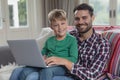 Father and son looking at camera while using laptop on sofa in a comfortable home Royalty Free Stock Photo